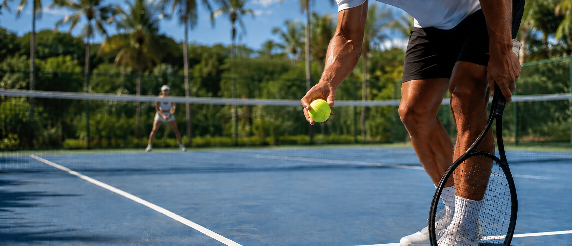 A player about to serve, holding a tennis ball at the net, with a doubles partner ready on the far side of the court.